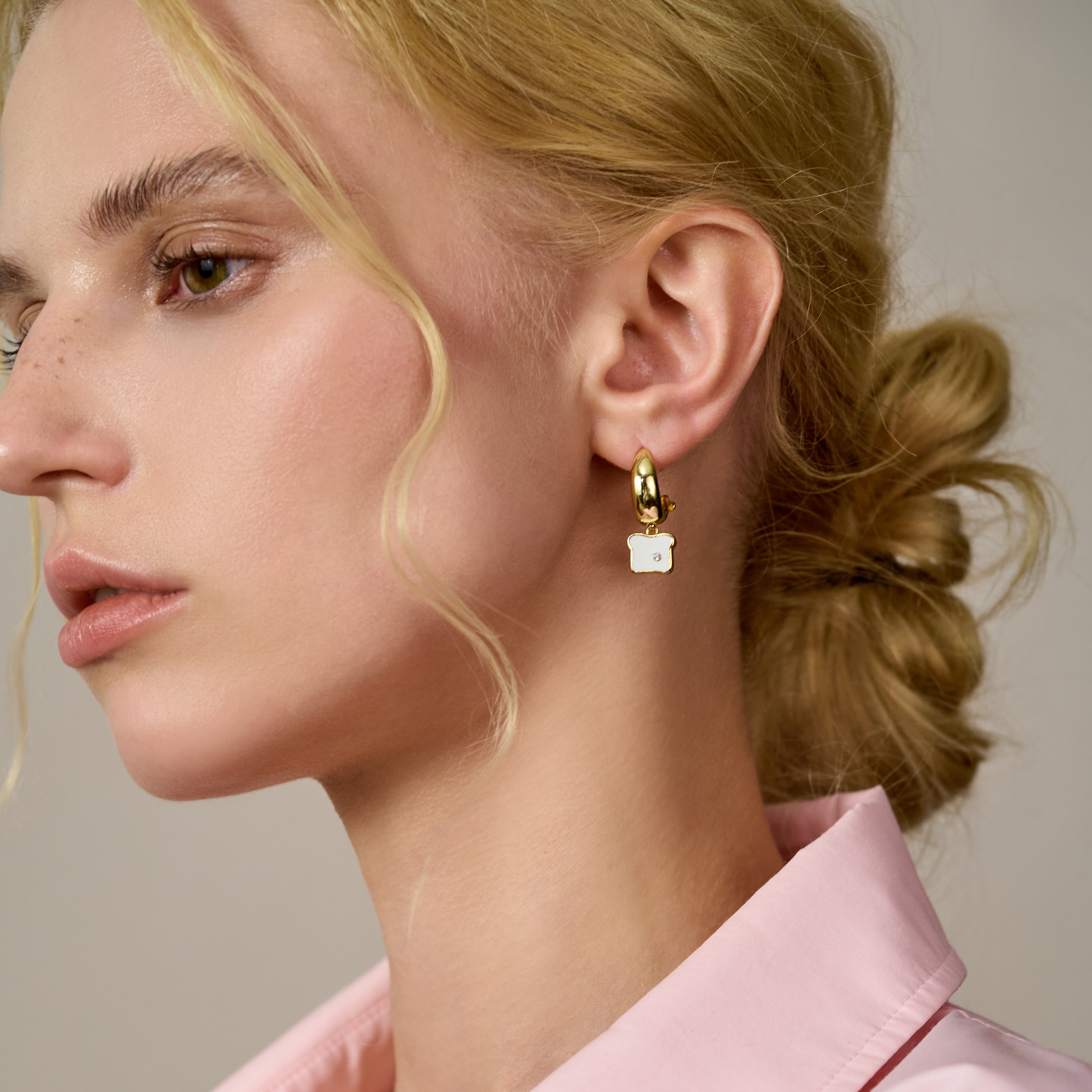 Woman wearing gold-plated hoop earring with white enamel charm, elegant jewelry style