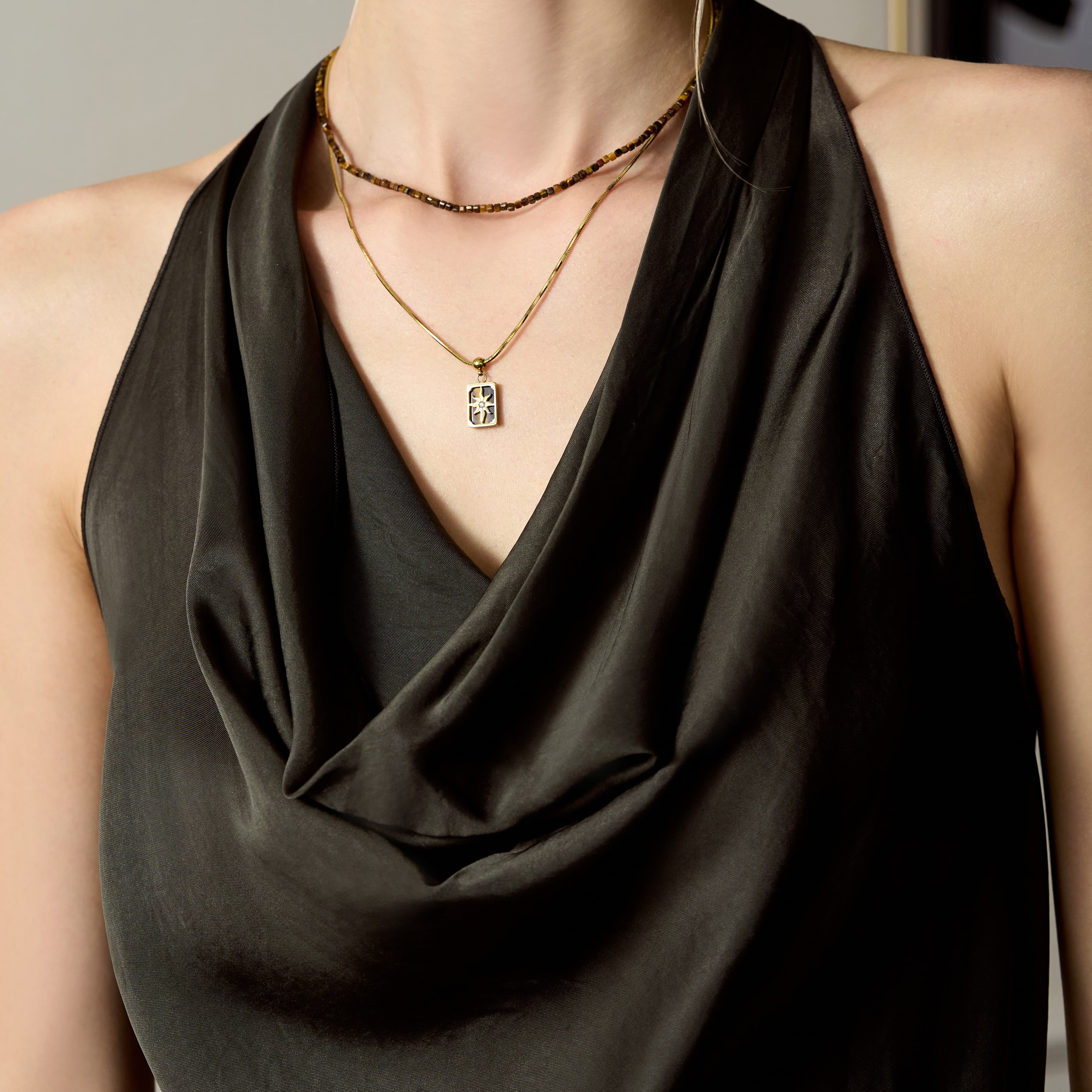 Woman wearing layered gold-plated necklaces with a pendant and beaded choker, black draped top
