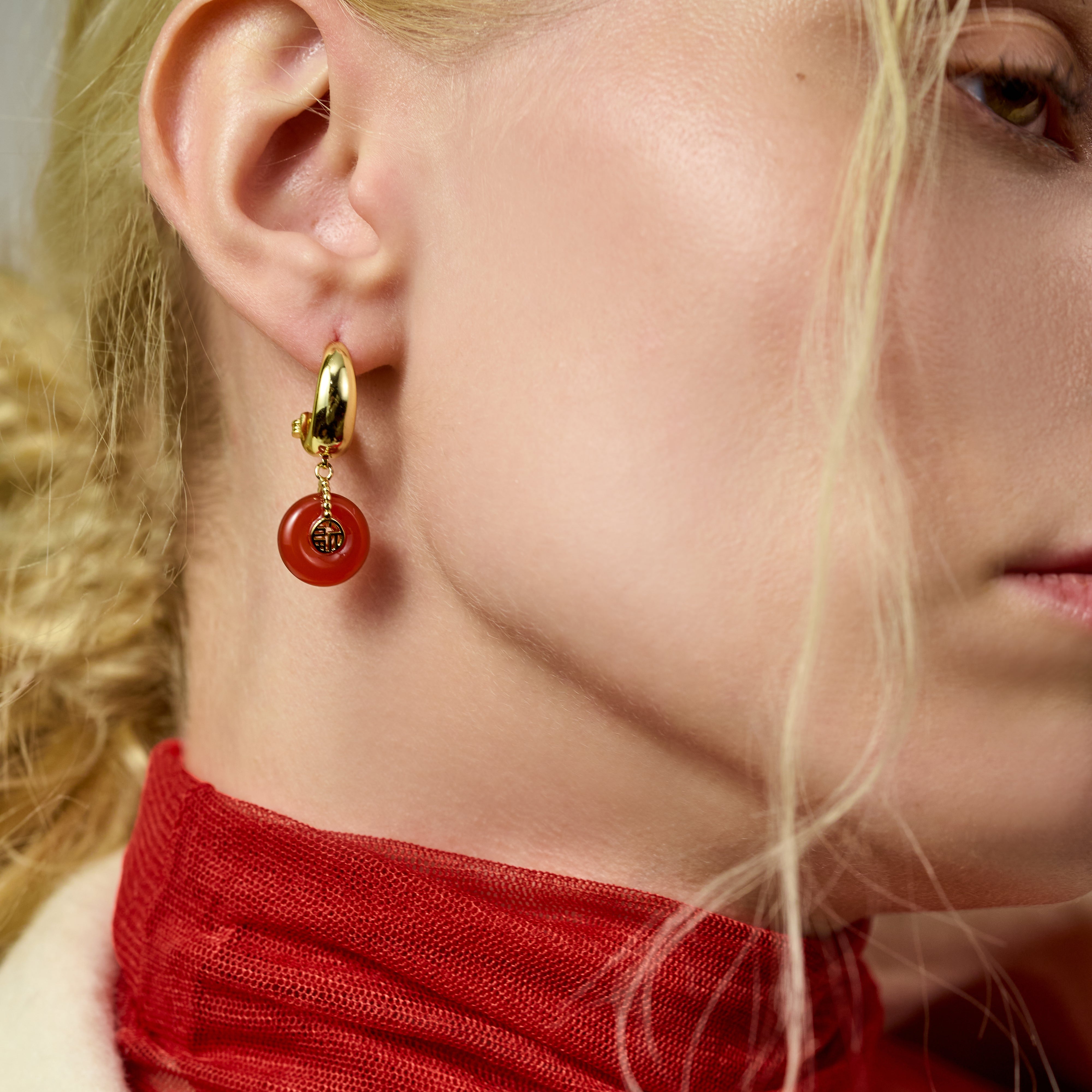 Gold-plated hoop earring with red circular pendant on woman wearing a red scarf