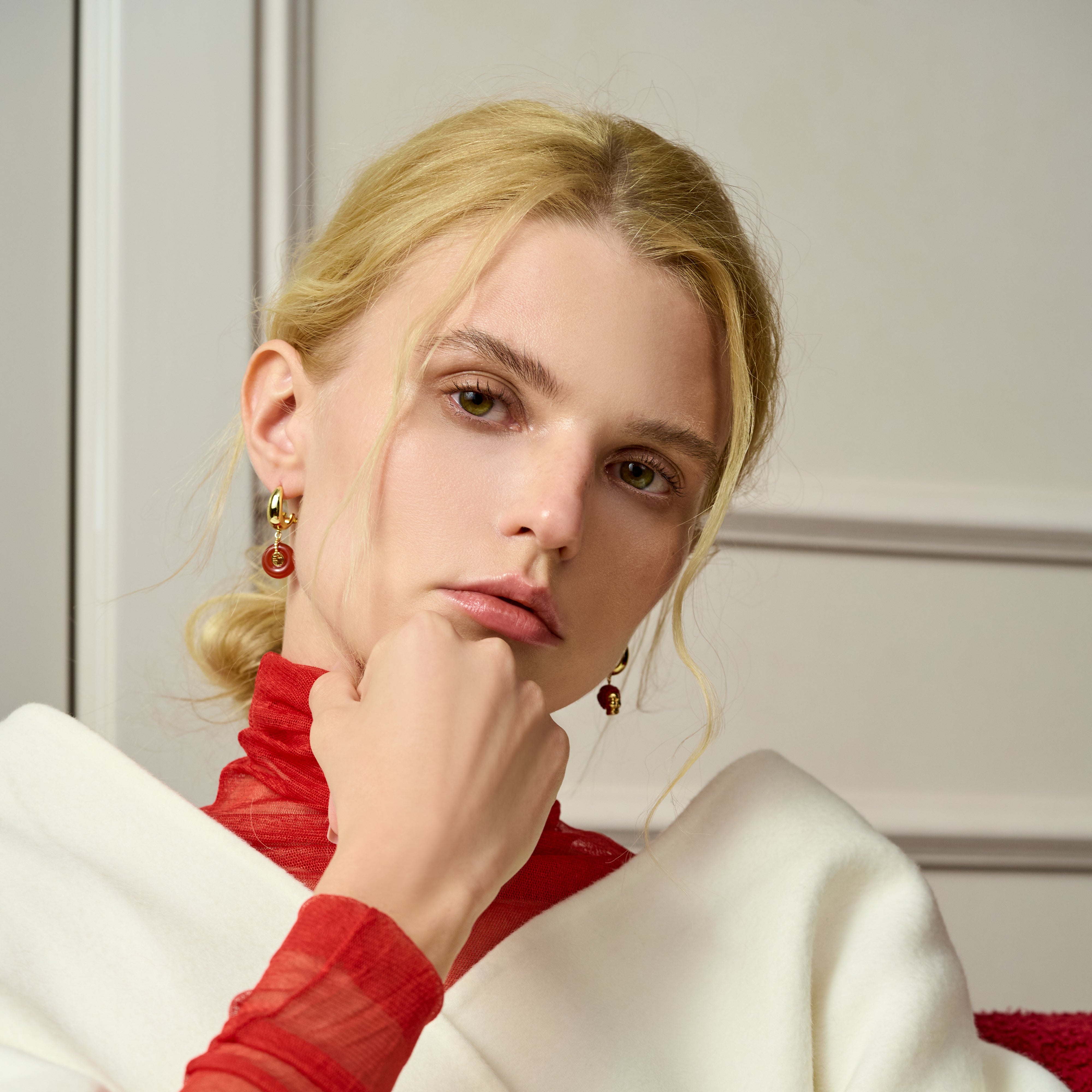 Woman wearing gold-plated drop earrings and a red sheer turtleneck top