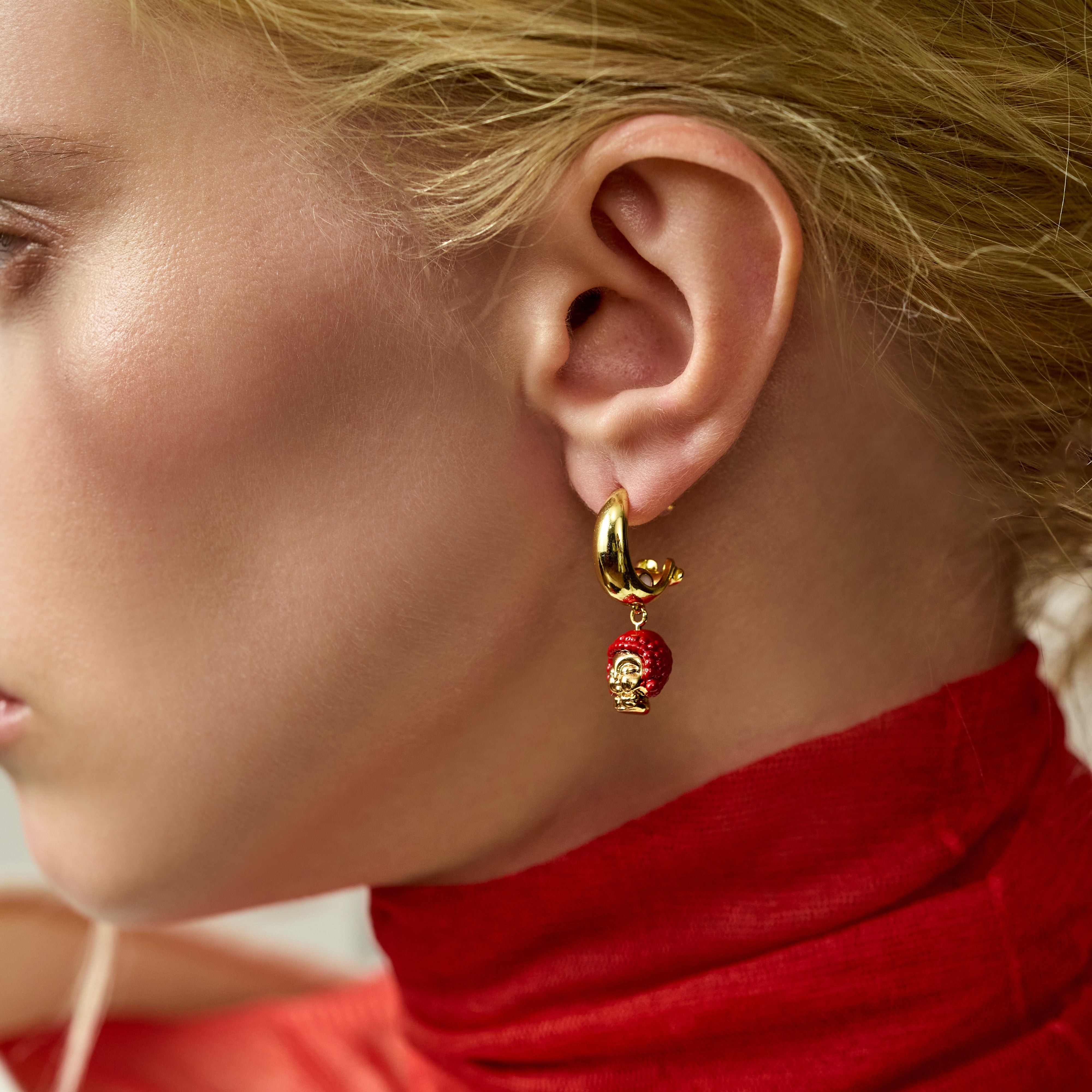 Gold-plated hoop earring with red beaded charm on woman in red turtleneck