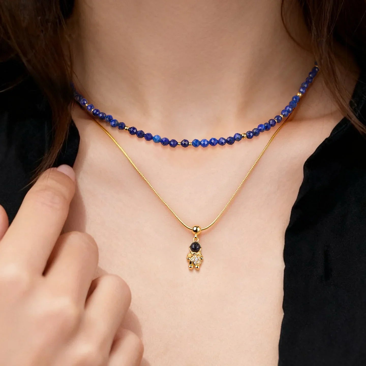 Woman wearing layered gold-plated pendant necklace and blue beaded choker with black top.