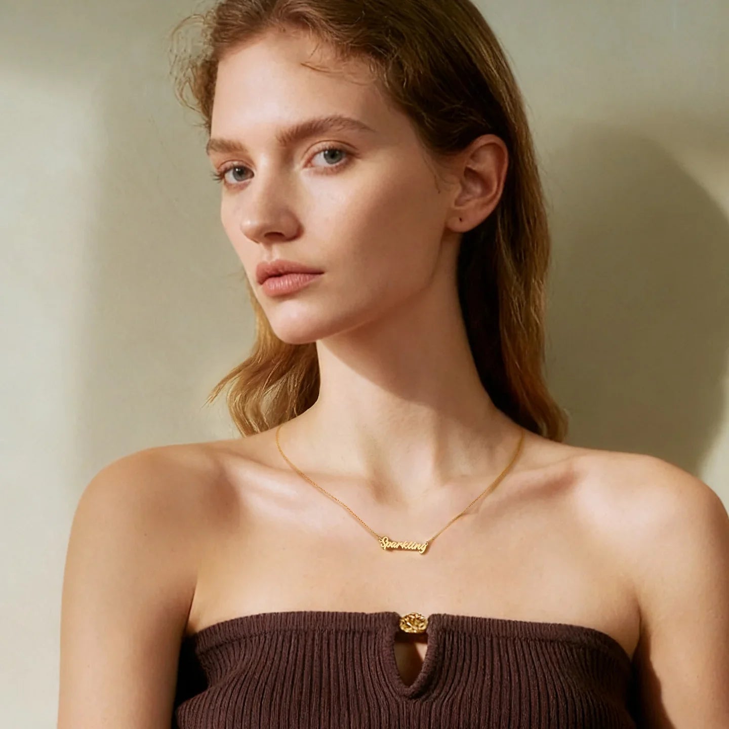 Woman wearing a gold-plated name necklace and brown strapless top, elegant jewelry style