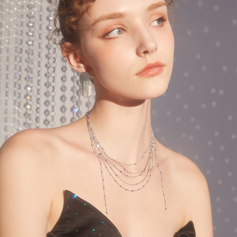 Woman wearing layered silver necklace and statement silver earring in elegant dress