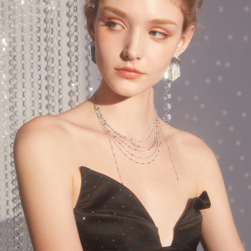 Woman wearing layered silver necklace and statement earrings in elegant black dress