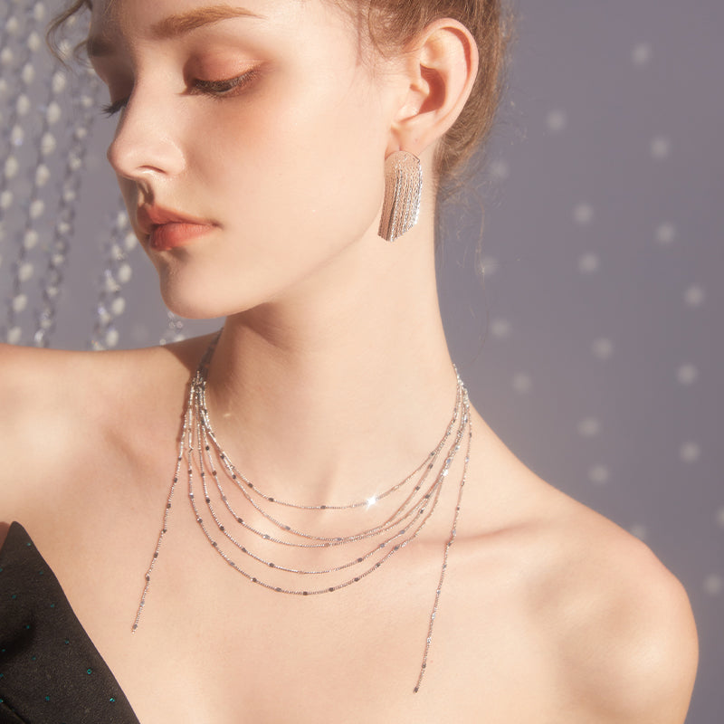Woman wearing layered silver necklace and crystal statement earrings, elegant style