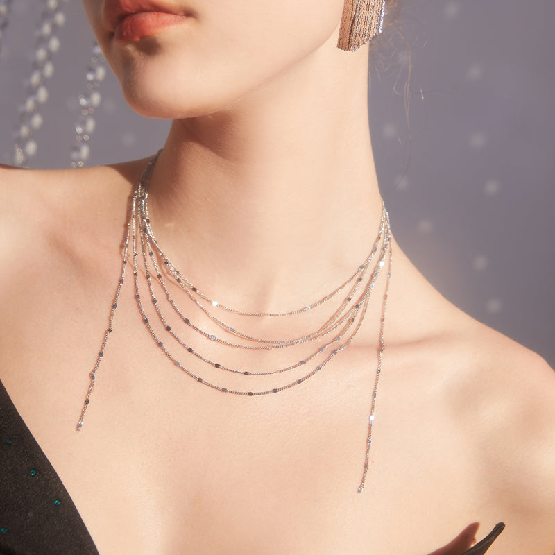 Woman wearing layered silver chain necklace and statement drop earring, elegant jewelry fashion