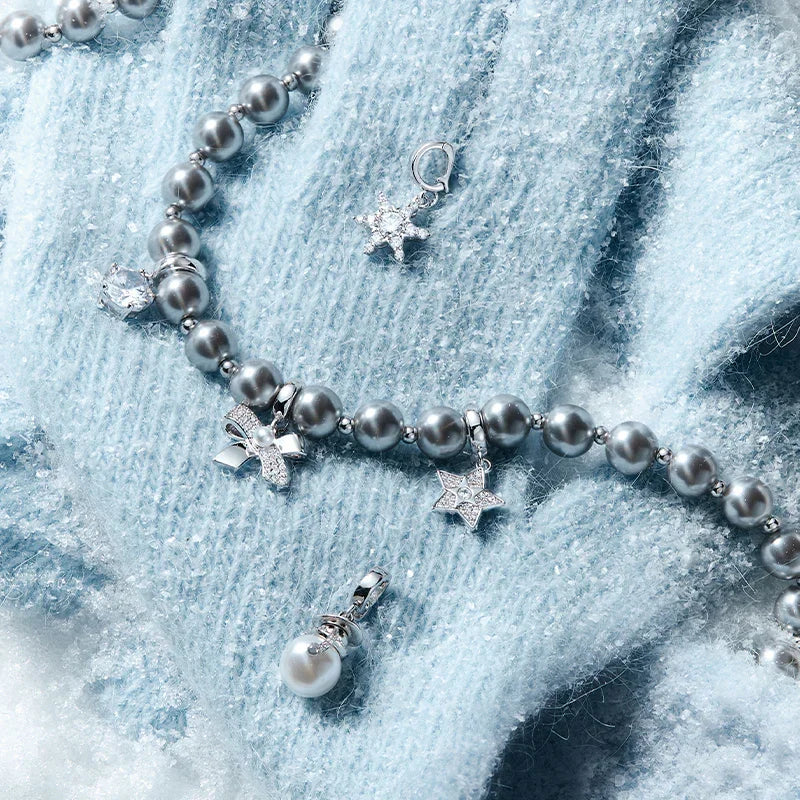 Silver-gray pearl necklace with star, bow, and pearl charms on a soft blue knit background