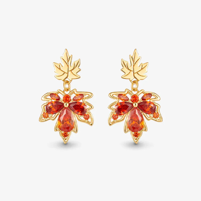Gold-plated leaf earrings with red gemstone accents, statement dangle jewelry on white background.