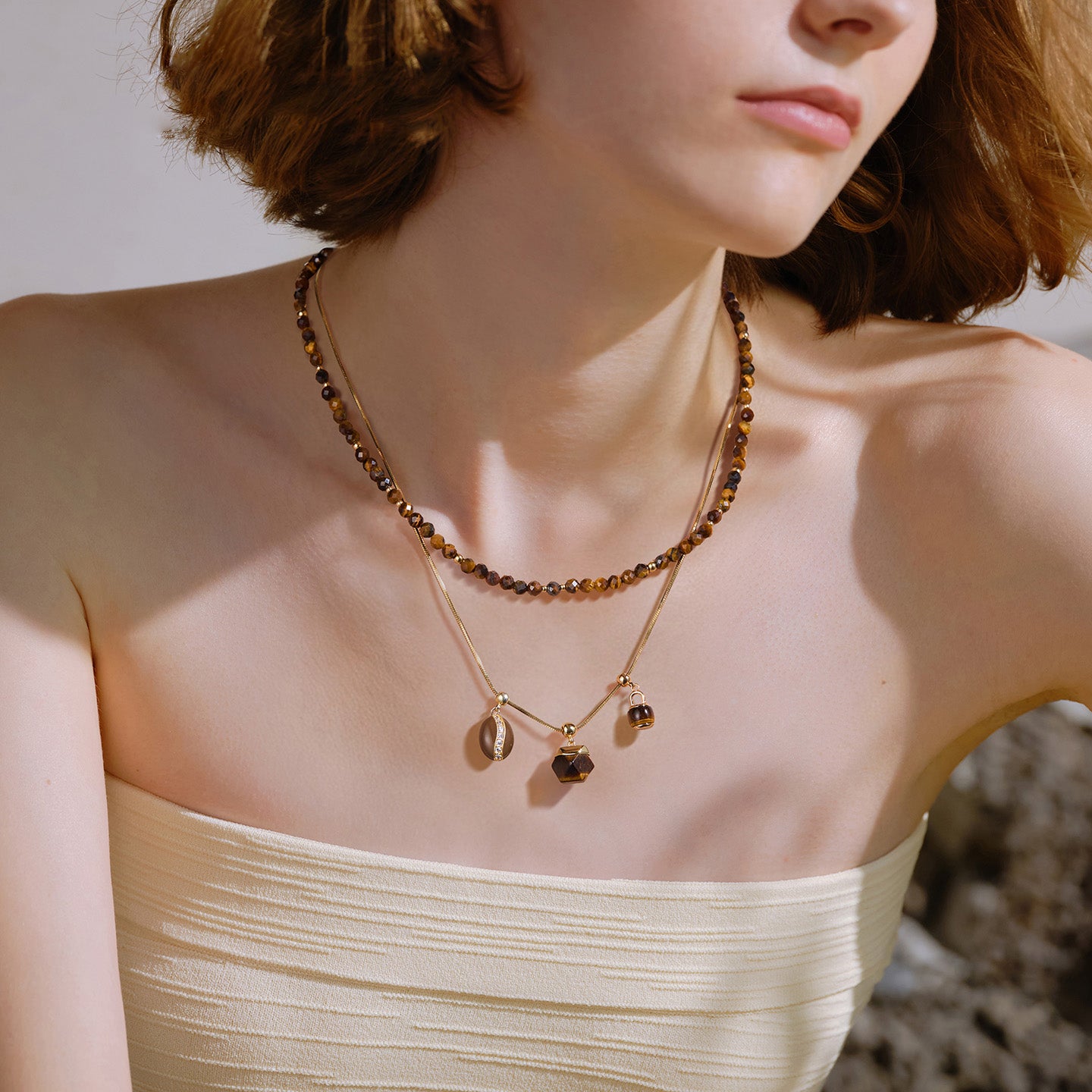 Woman wearing layered gold-plated gemstone necklaces and a cream strapless top