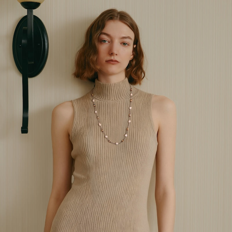 Woman wearing a sleeveless beige knit dress and a gold-plated beaded necklace