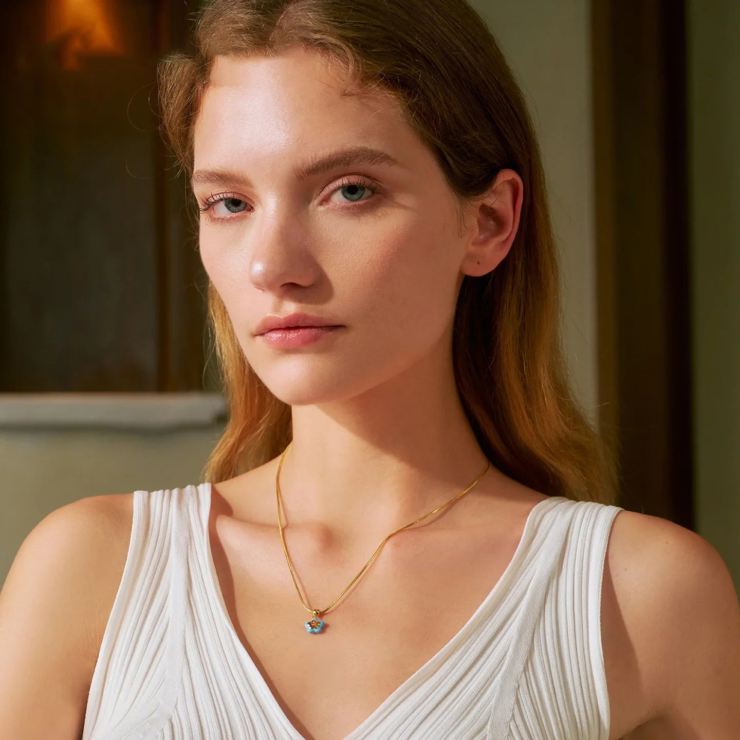 Woman wearing gold-plated necklace with blue flower pendant, white sleeveless top