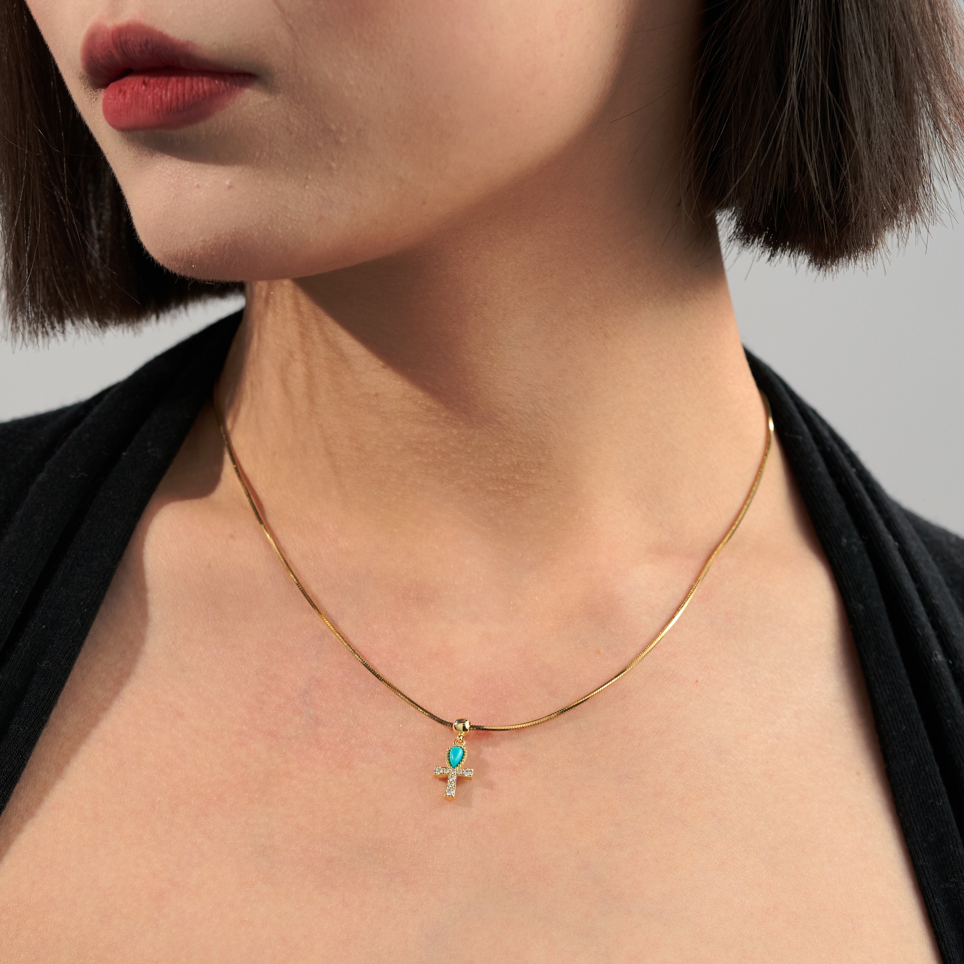 Gold-plated necklace with turquoise cross pendant on woman's neck, elegant jewelry style