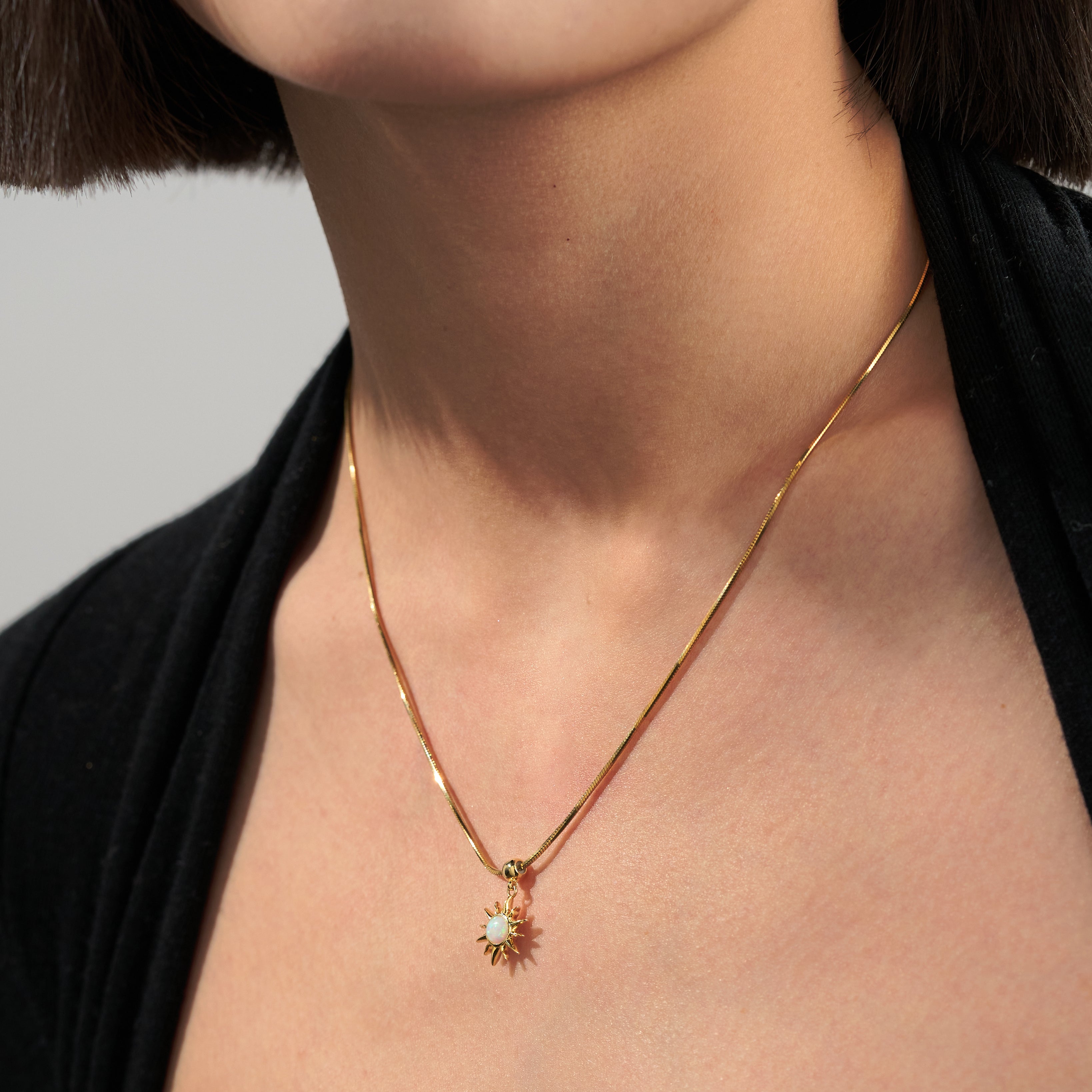 Woman wearing gold-plated necklace with sunburst pendant and opal accent