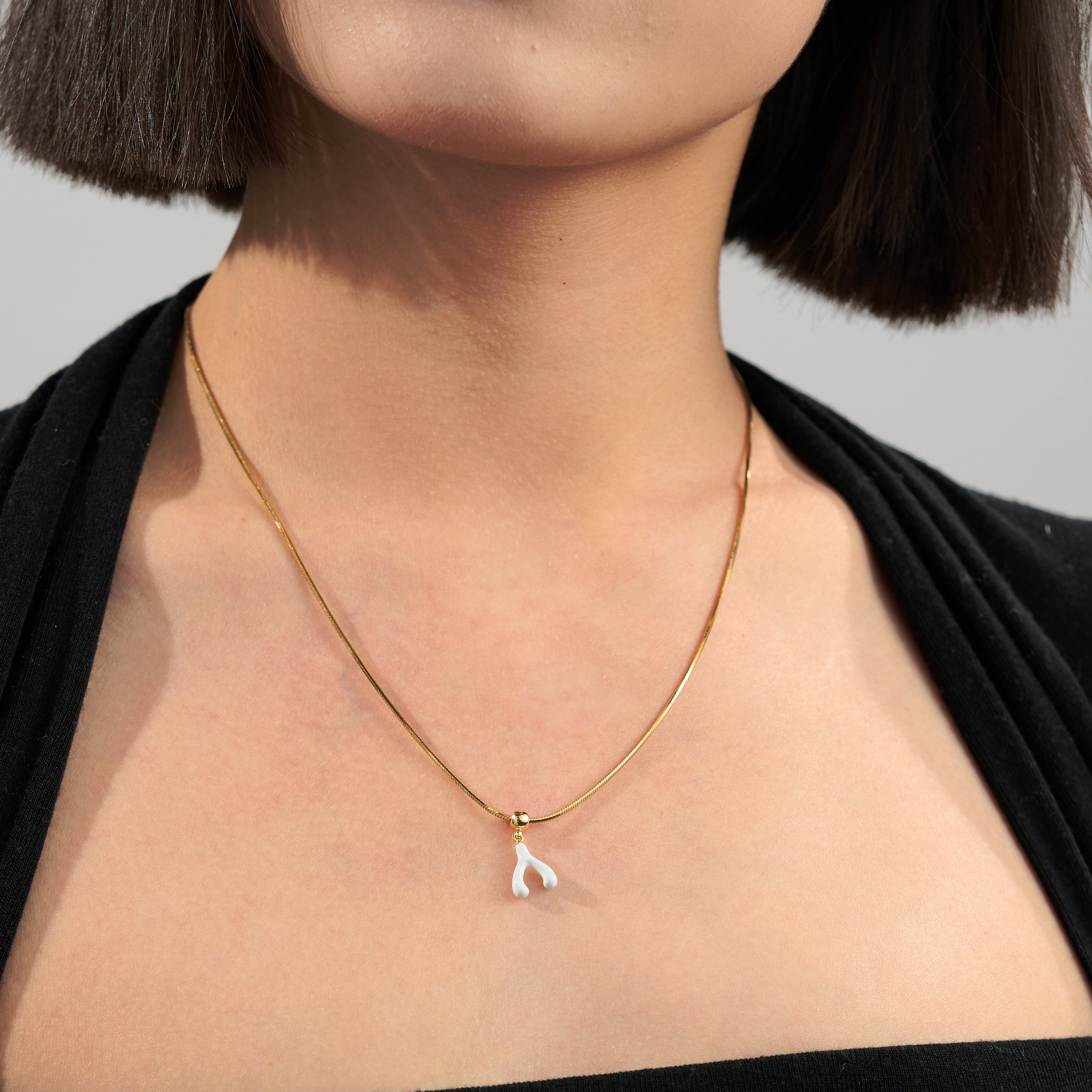 Gold-plated necklace with delicate white wishbone pendant on woman's neck