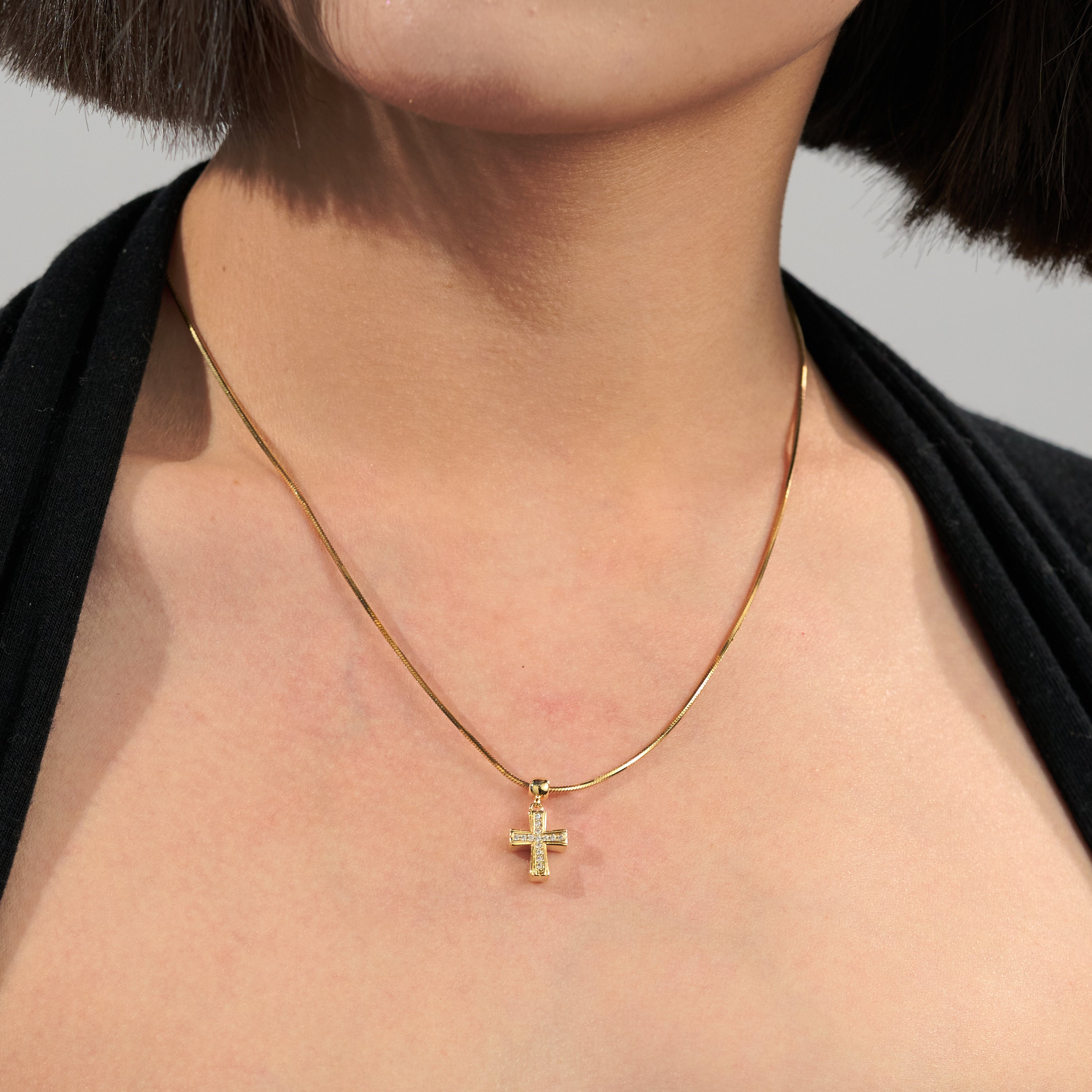 Gold-plated cross pendant necklace on woman with short dark hair and black top