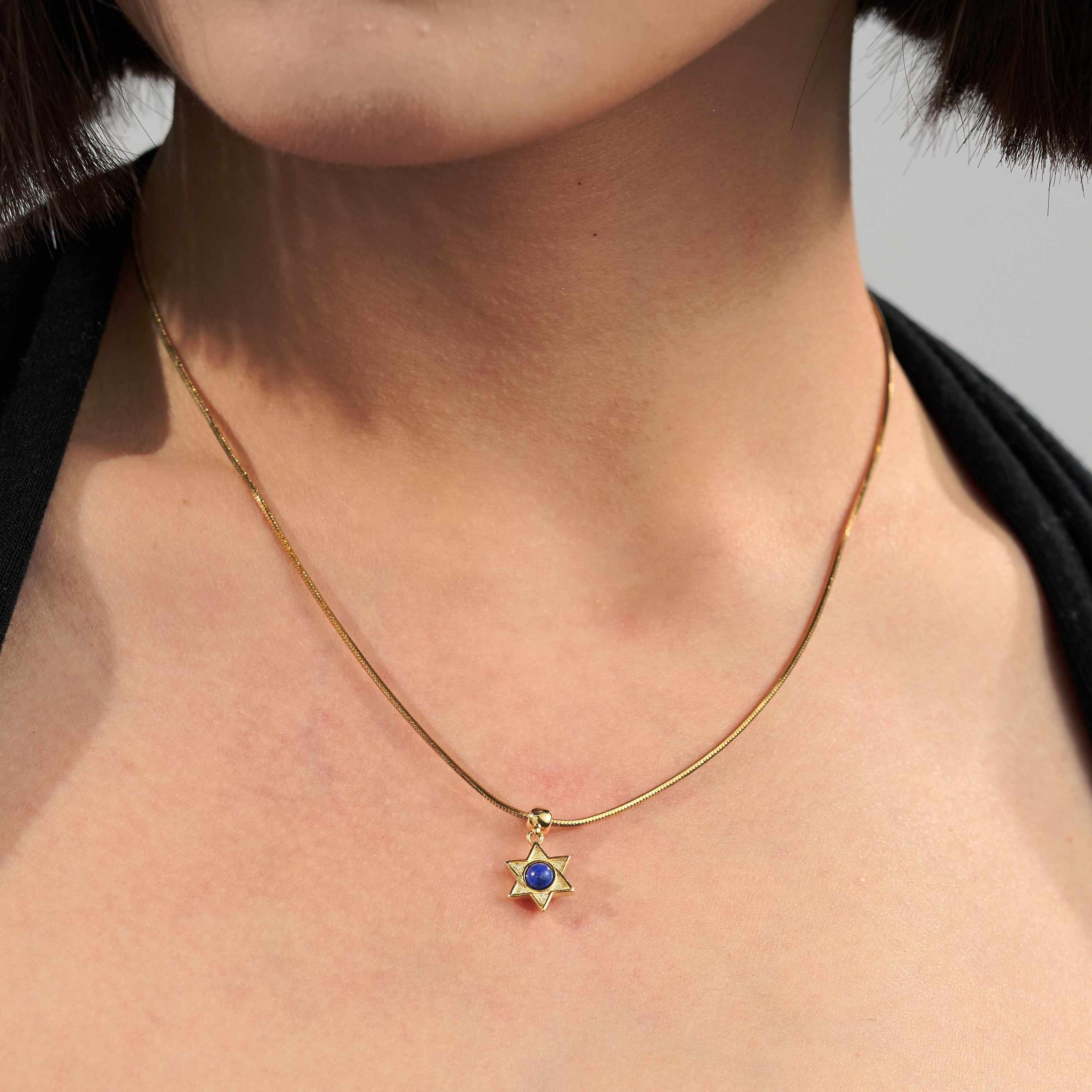 Gold-plated necklace with star-shaped blue gemstone pendant on a woman's neck