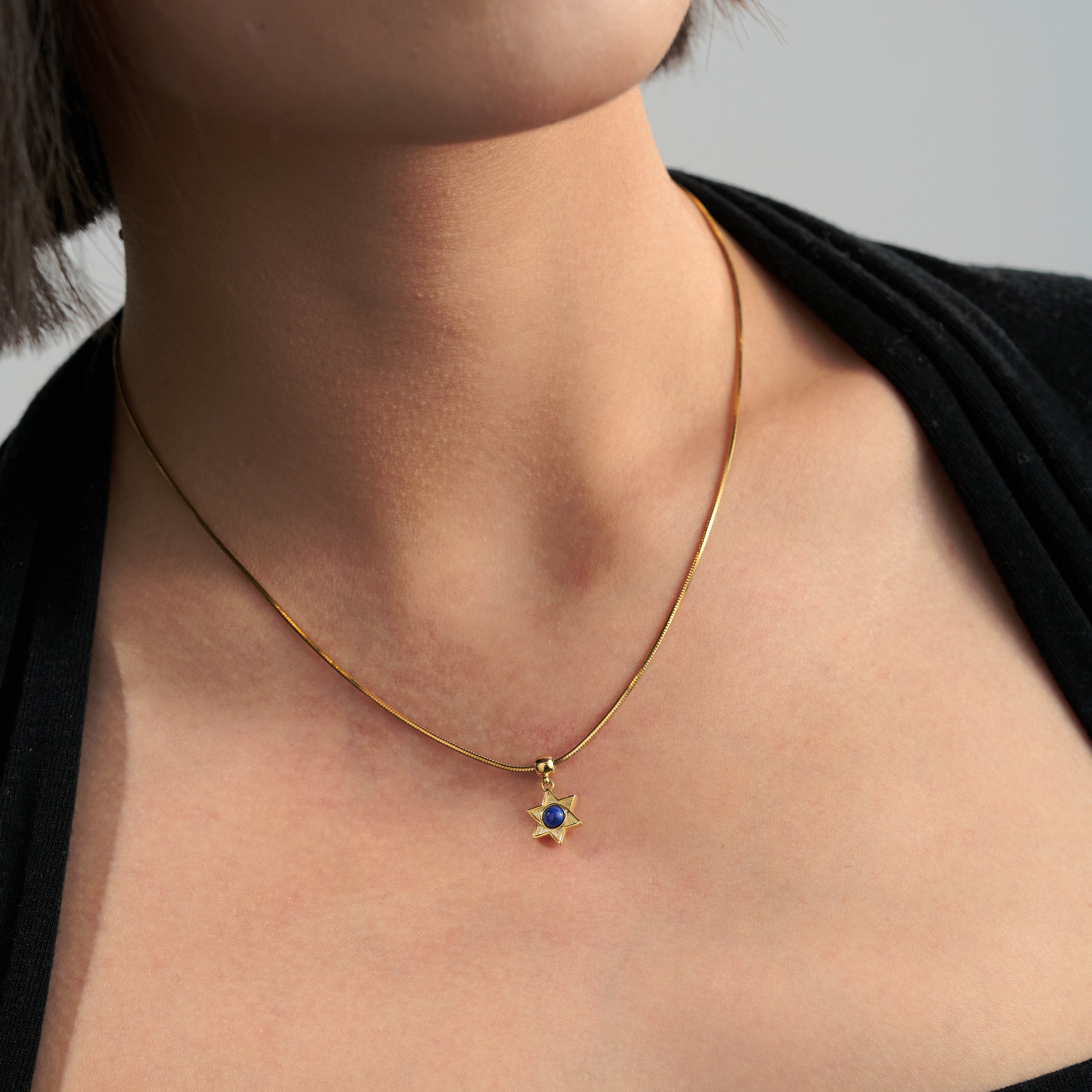 Gold-plated star pendant necklace with blue stone on woman’s neck