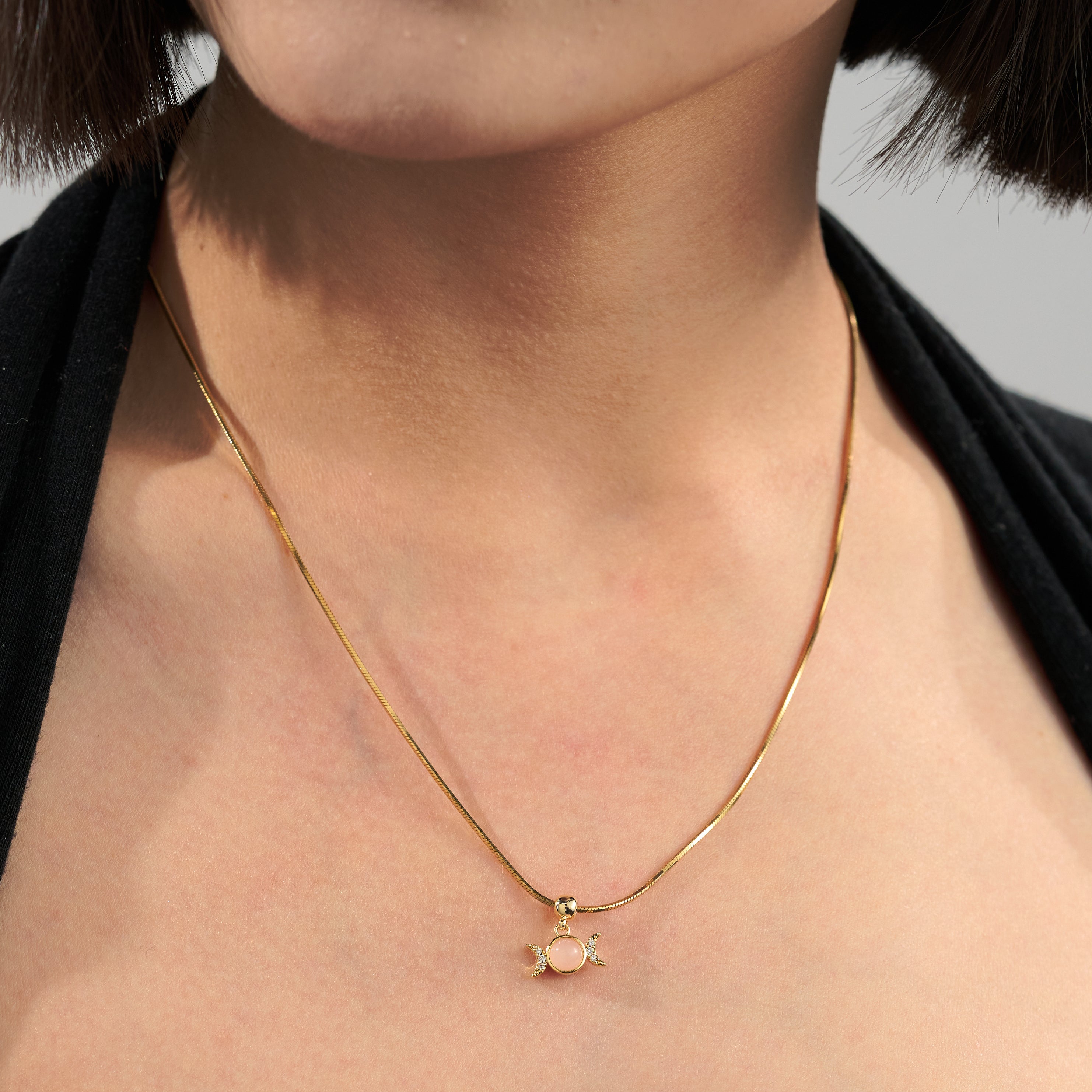 Gold-plated necklace with pink gemstone pendant on woman's neck, elegant jewelry