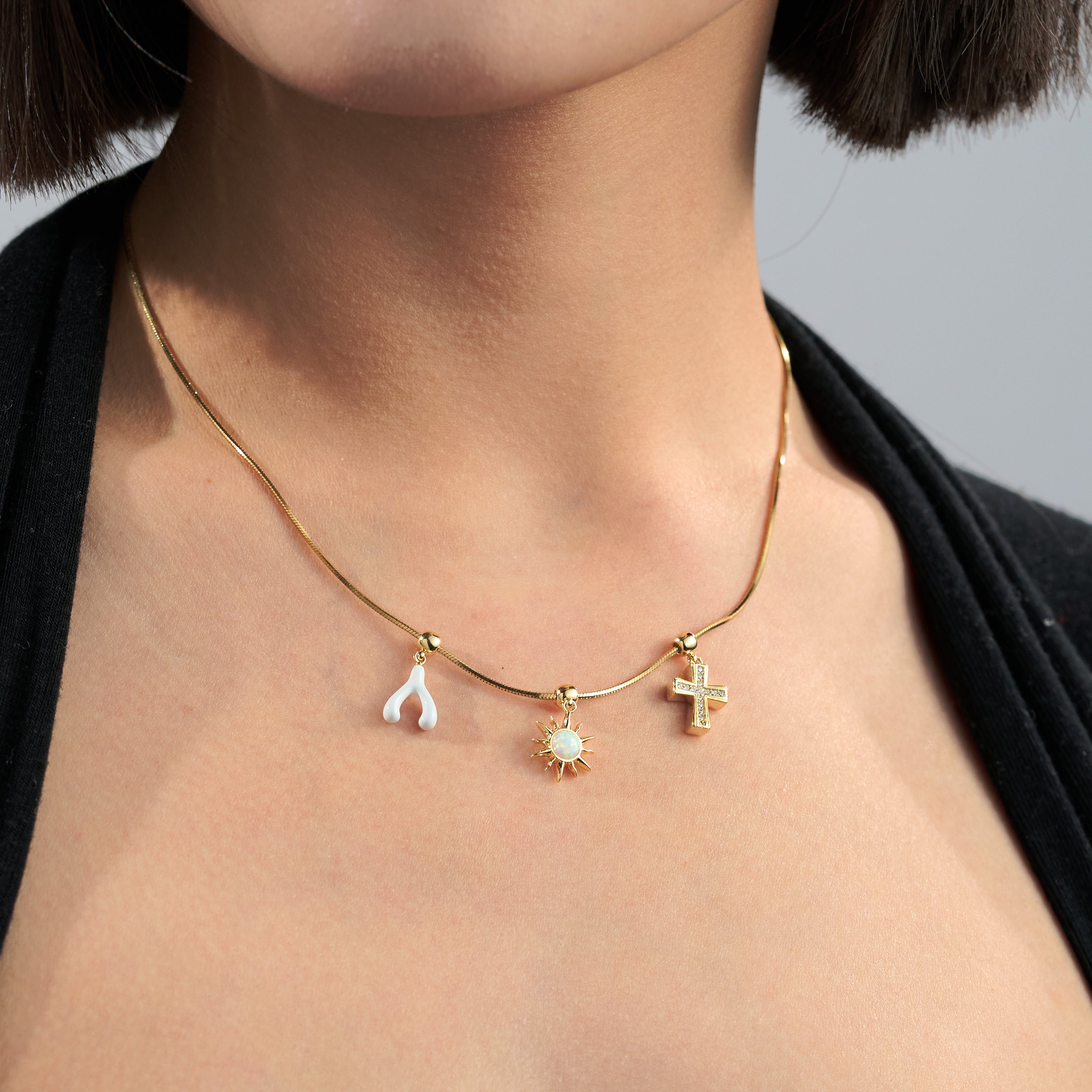 Gold-plated necklace with sun, cross, and wishbone pendants on woman's neck