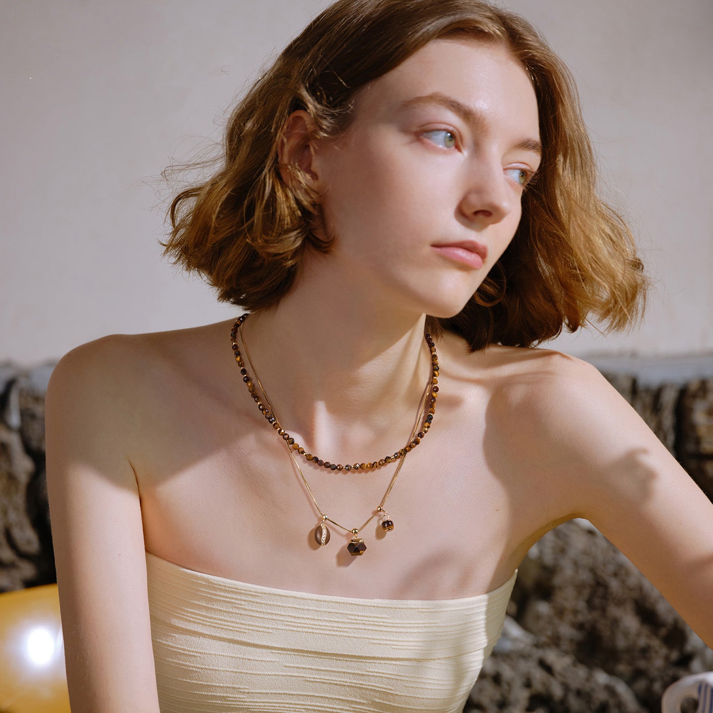 Woman wearing layered gold-plated necklaces with brown beads and charms, elegant style