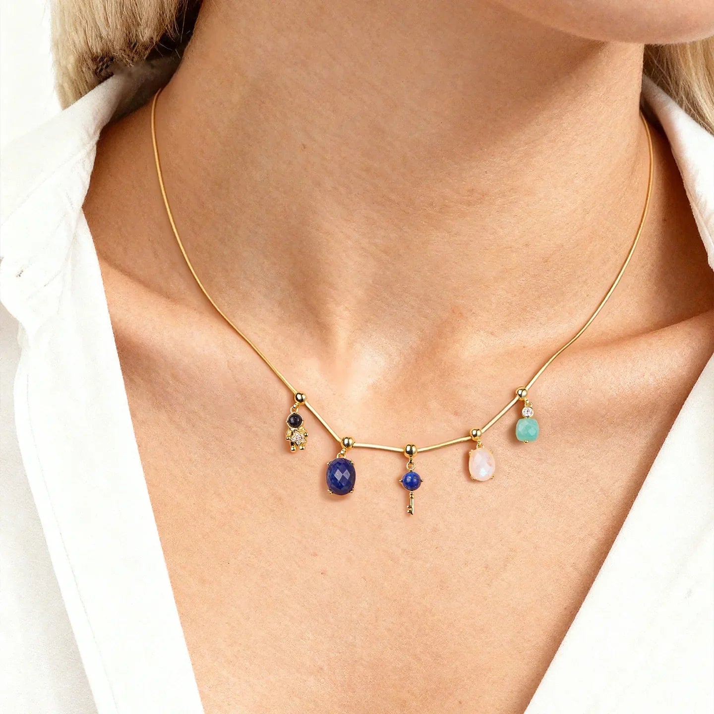 Gold-plated necklace with colorful gemstone pendants on a woman in a white blouse