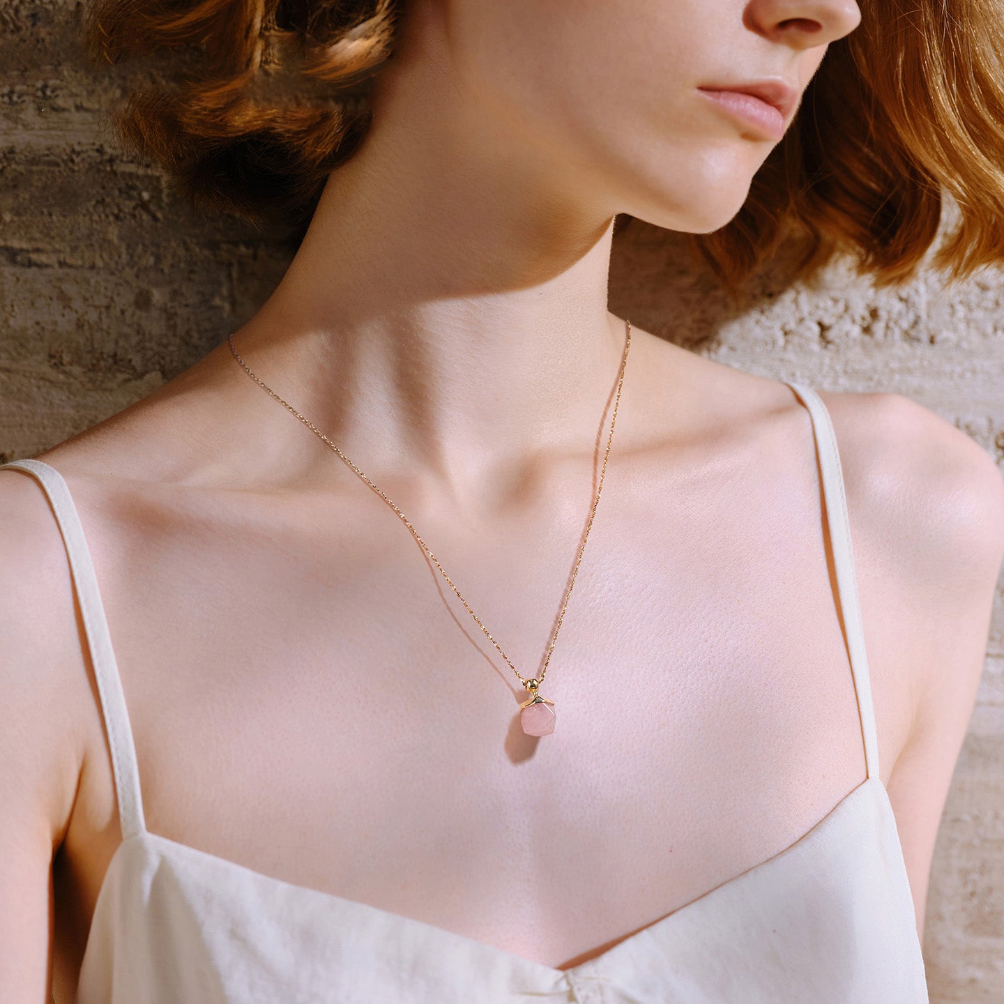 Woman wearing gold-plated necklace with pink stone pendant, minimalist summer style