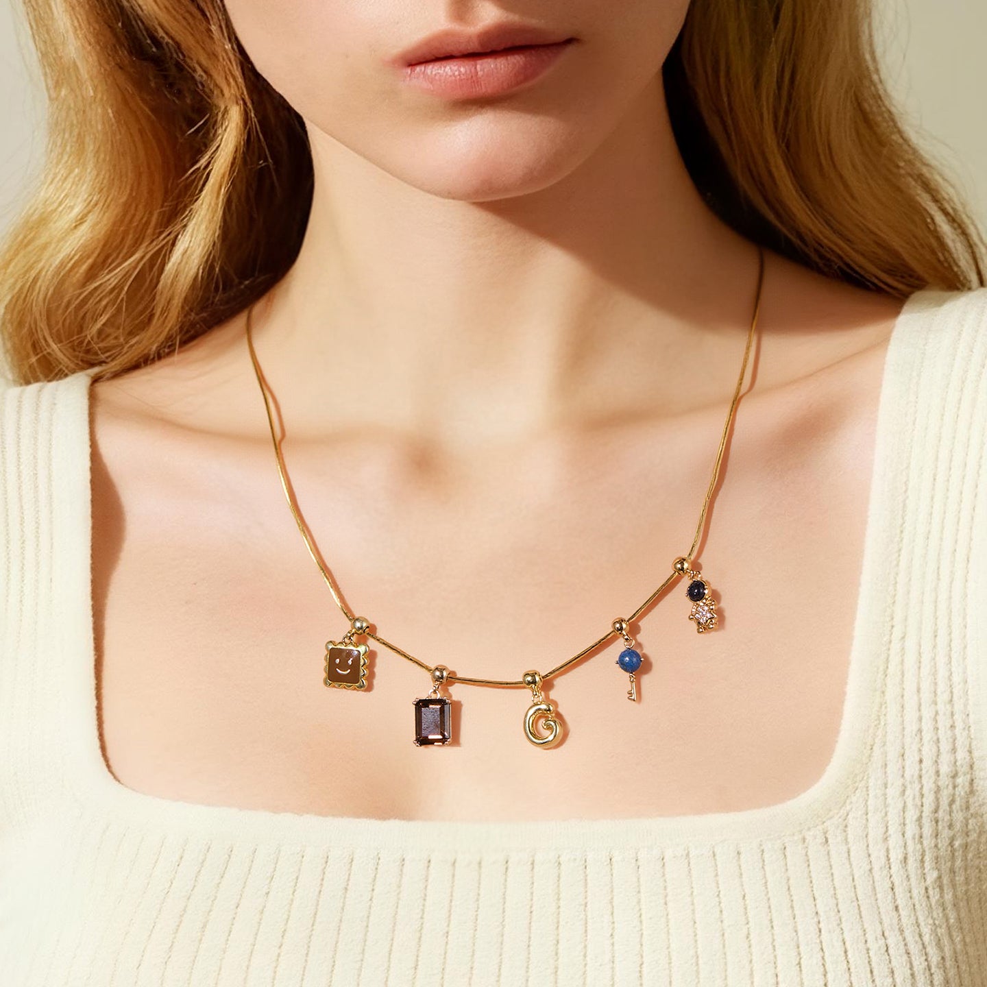 Gold-plated charm necklace with varied pendants on a woman in a cream ribbed top