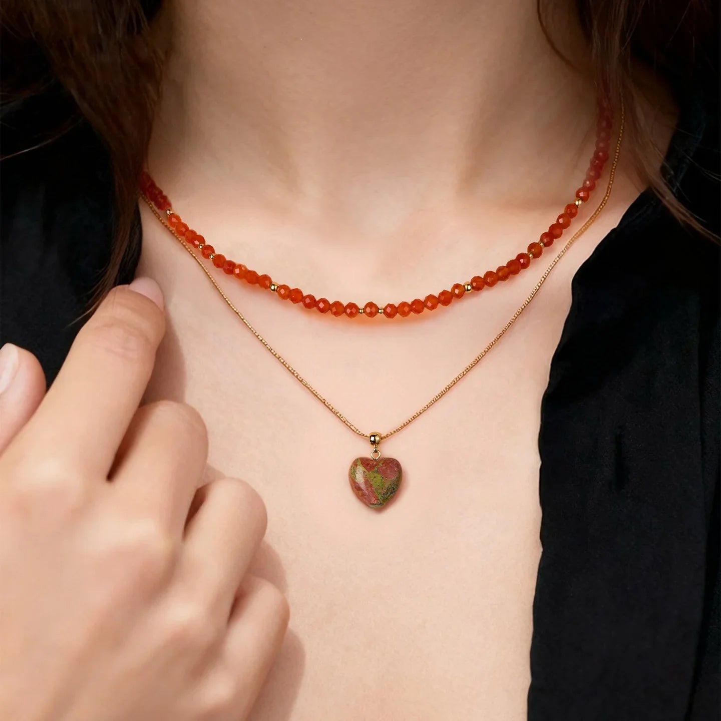 Woman wearing layered necklaces, red beaded choker and gold heart pendant, black top