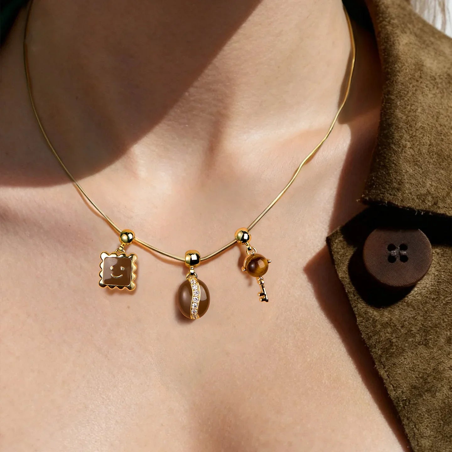 Gold-plated necklace with three brown gemstone pendants on a woman's neck, suede jacket visible.