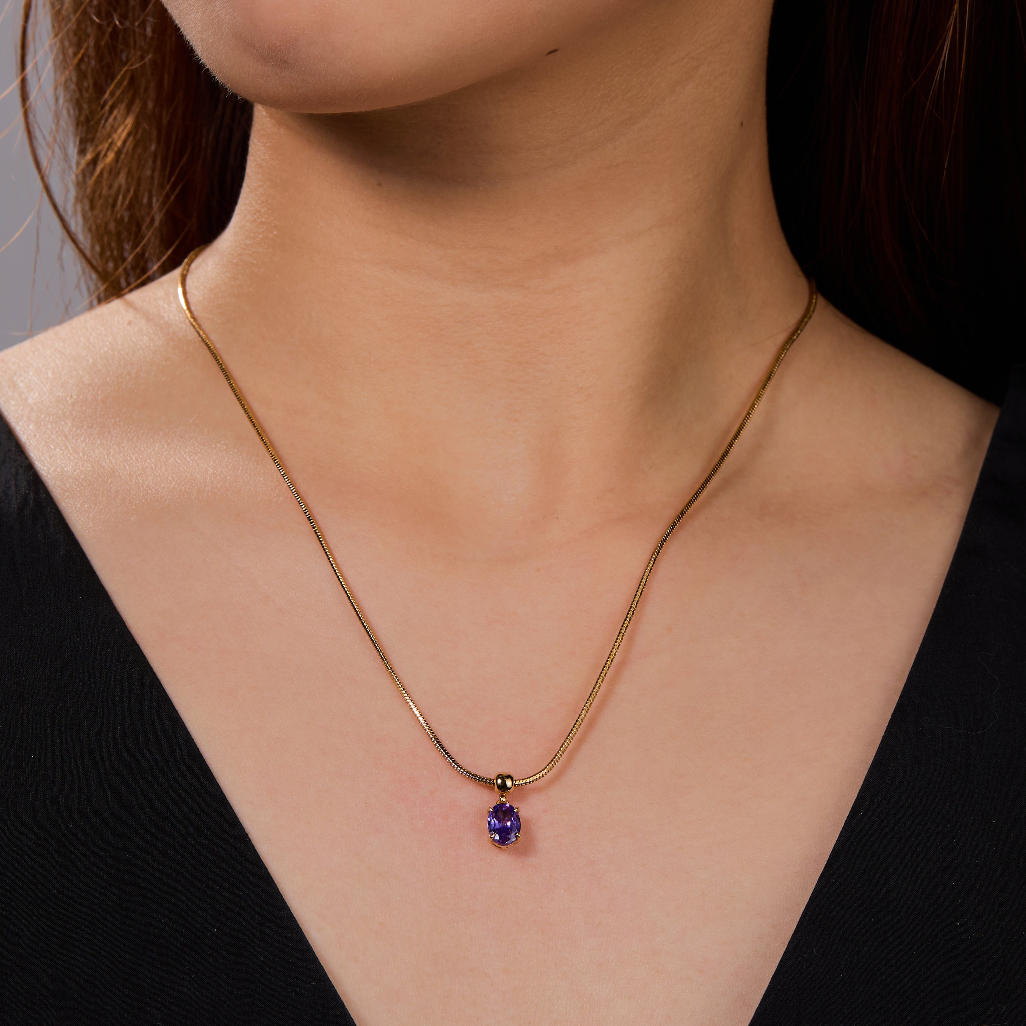 Gold-plated necklace with purple gemstone pendant on woman's neck, elegant jewelry