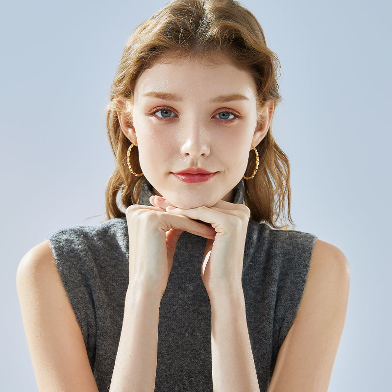 Woman wearing gold-plated statement hoop earrings and a sleeveless grey top