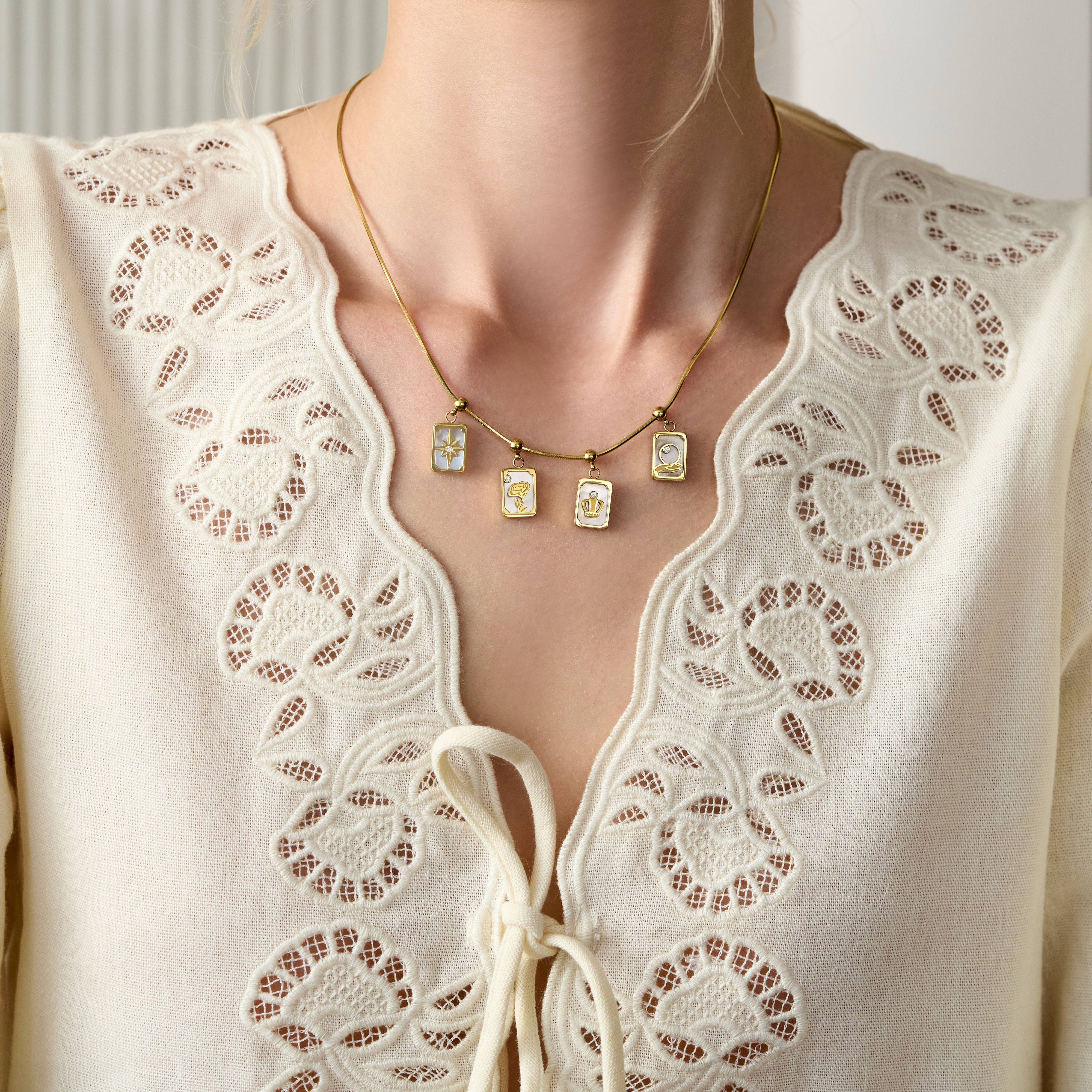 Gold-plated charm necklace with rectangular pendants, worn with a cream lace blouse.
