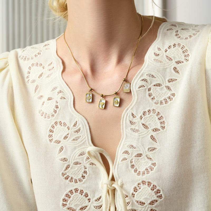 Woman wearing gold-plated charm necklace with four pendants, lace embroidered cream blouse