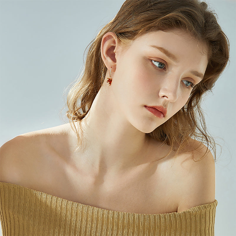 Woman wearing gold off-shoulder top and statement leaf drop earrings, elegant jewelry style