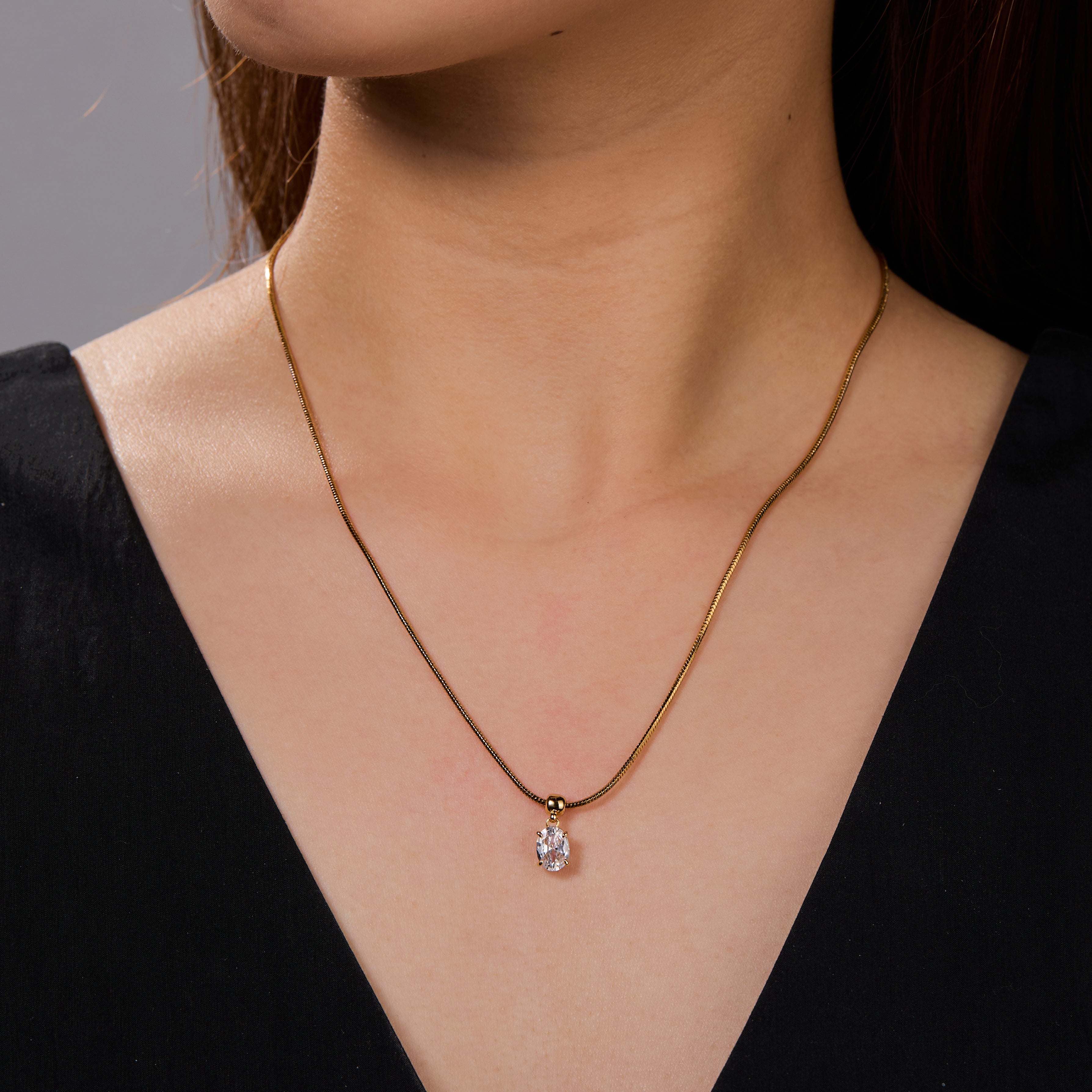 Gold-plated necklace with solitaire crystal pendant on woman's neck, elegant jewelry