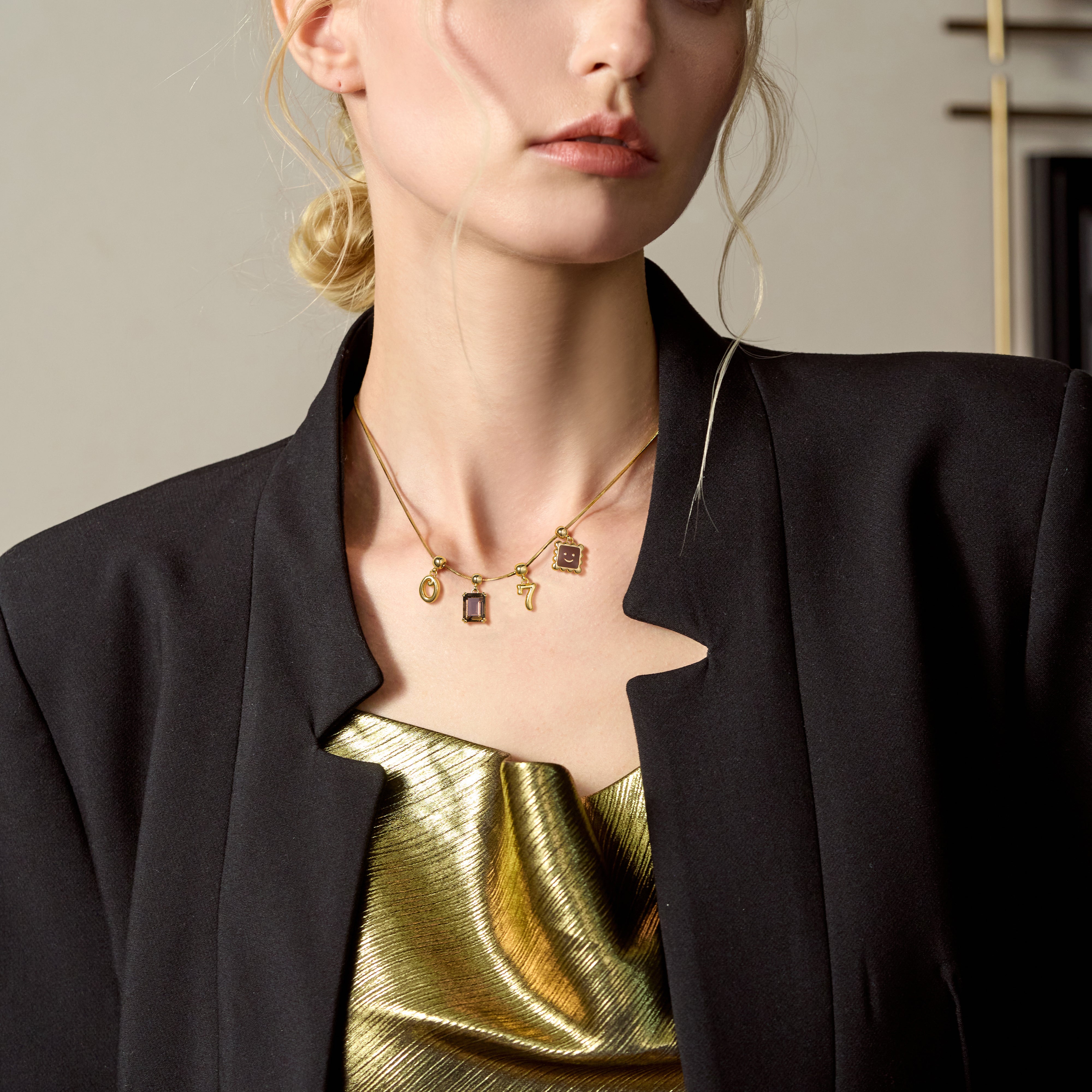 Woman wearing a gold-plated charm necklace with rectangular pendants and a black blazer.