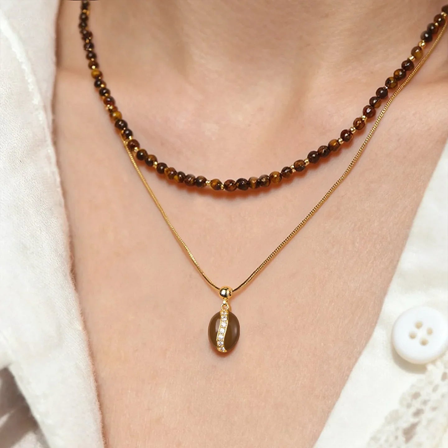 Layered gold-plated pendant necklace and brown beaded choker on woman's neck