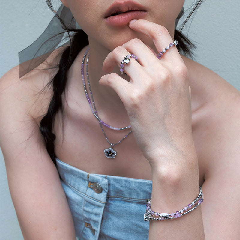 Woman wearing layered beaded necklaces, purple gemstone rings and bracelet, denim top