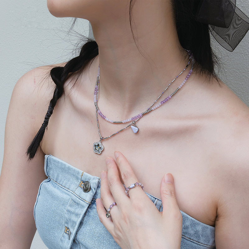 Woman wearing layered beaded necklaces and matching rings with purple accents, denim top