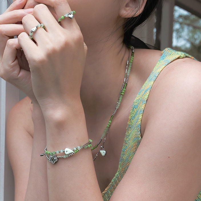 Woman wearing green beaded necklace, bracelet, and rings with heart charm detail