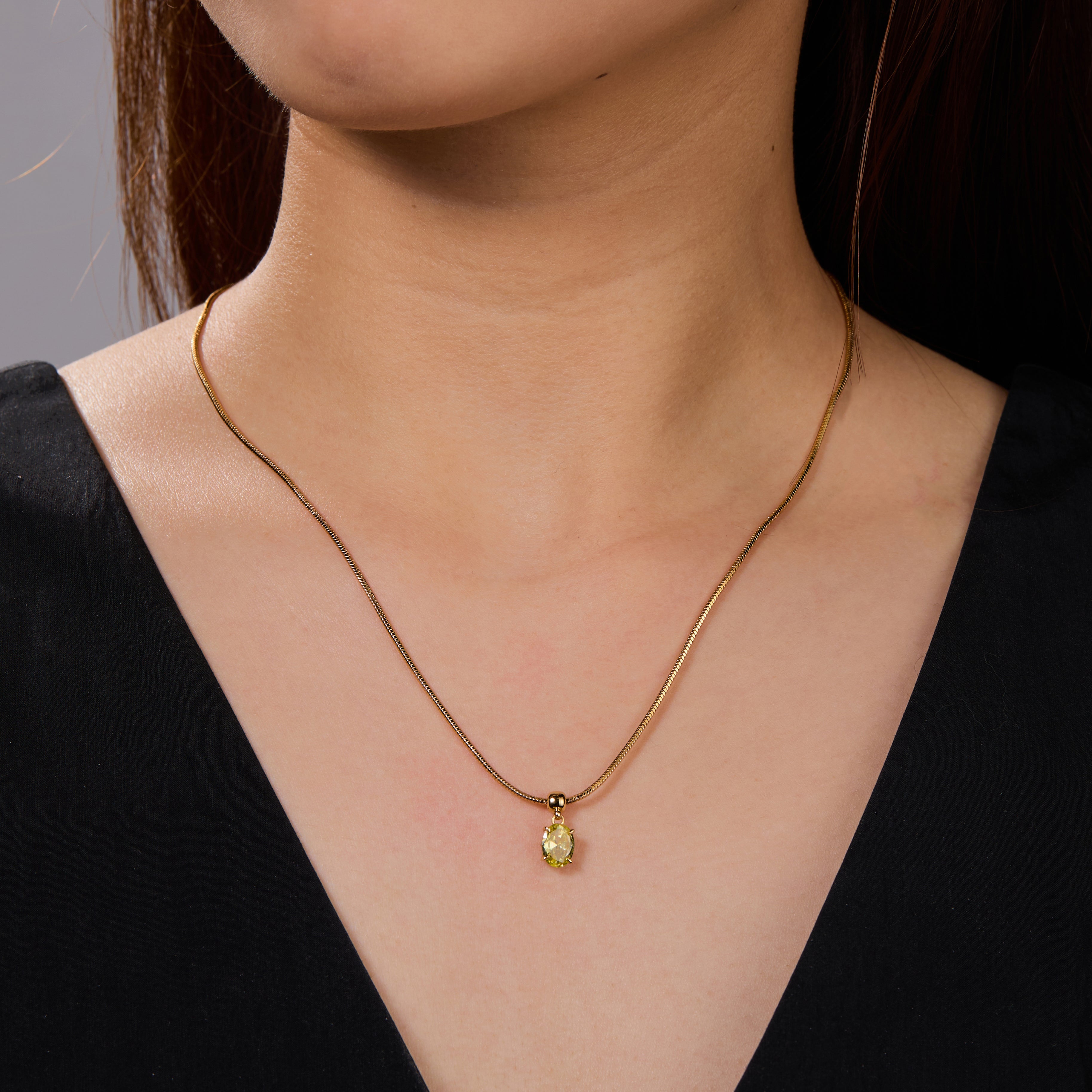 Gold-plated necklace with oval yellow gemstone pendant on woman wearing black top