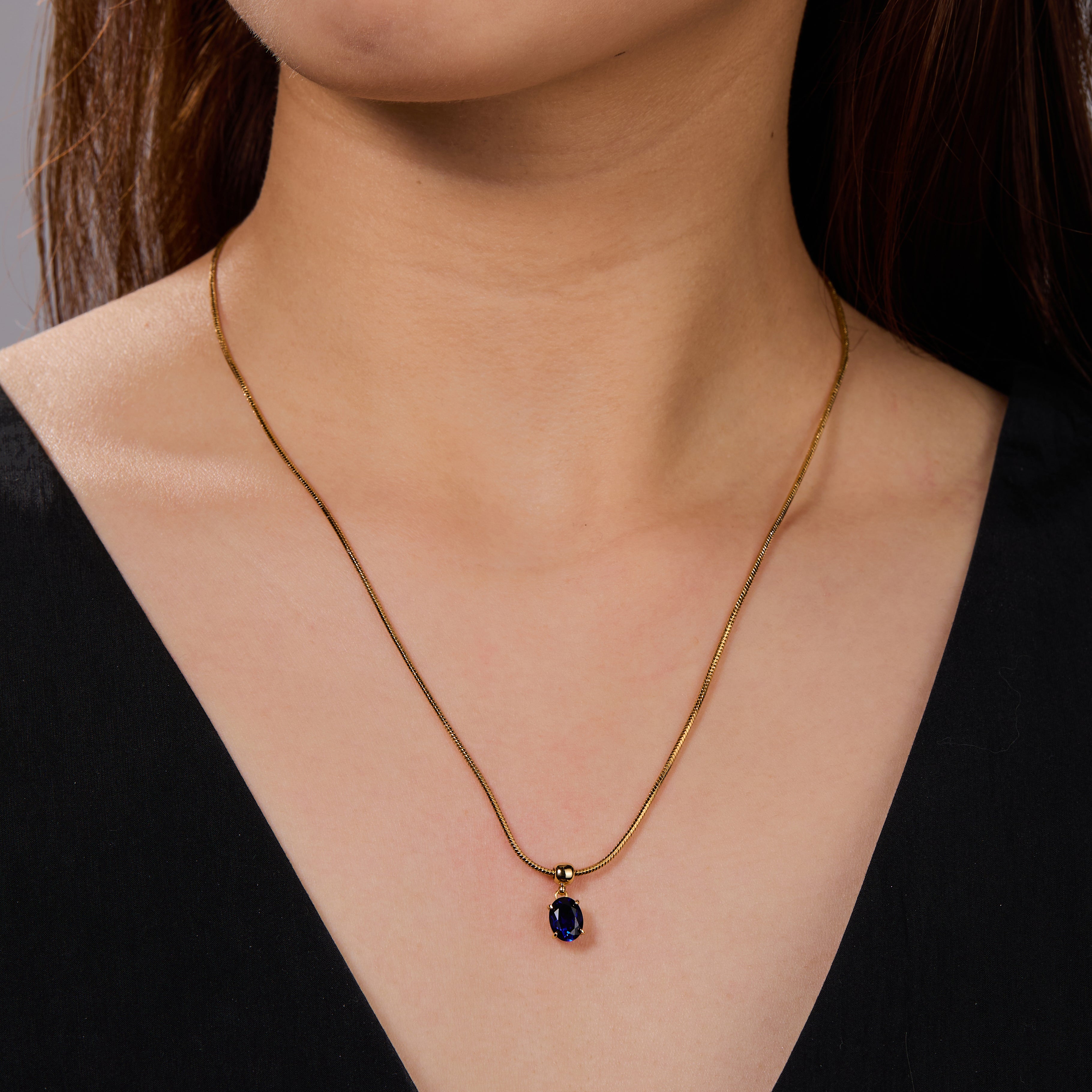 Gold-plated necklace with blue gemstone pendant on woman wearing black top