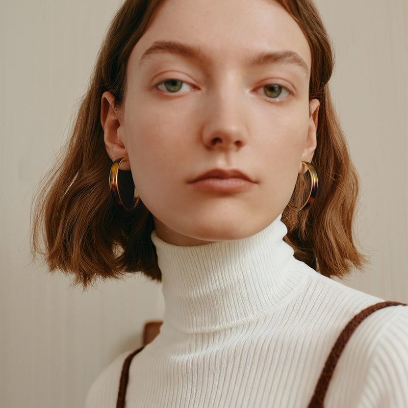 Woman wearing large gold hoop earrings and a white turtleneck sweater