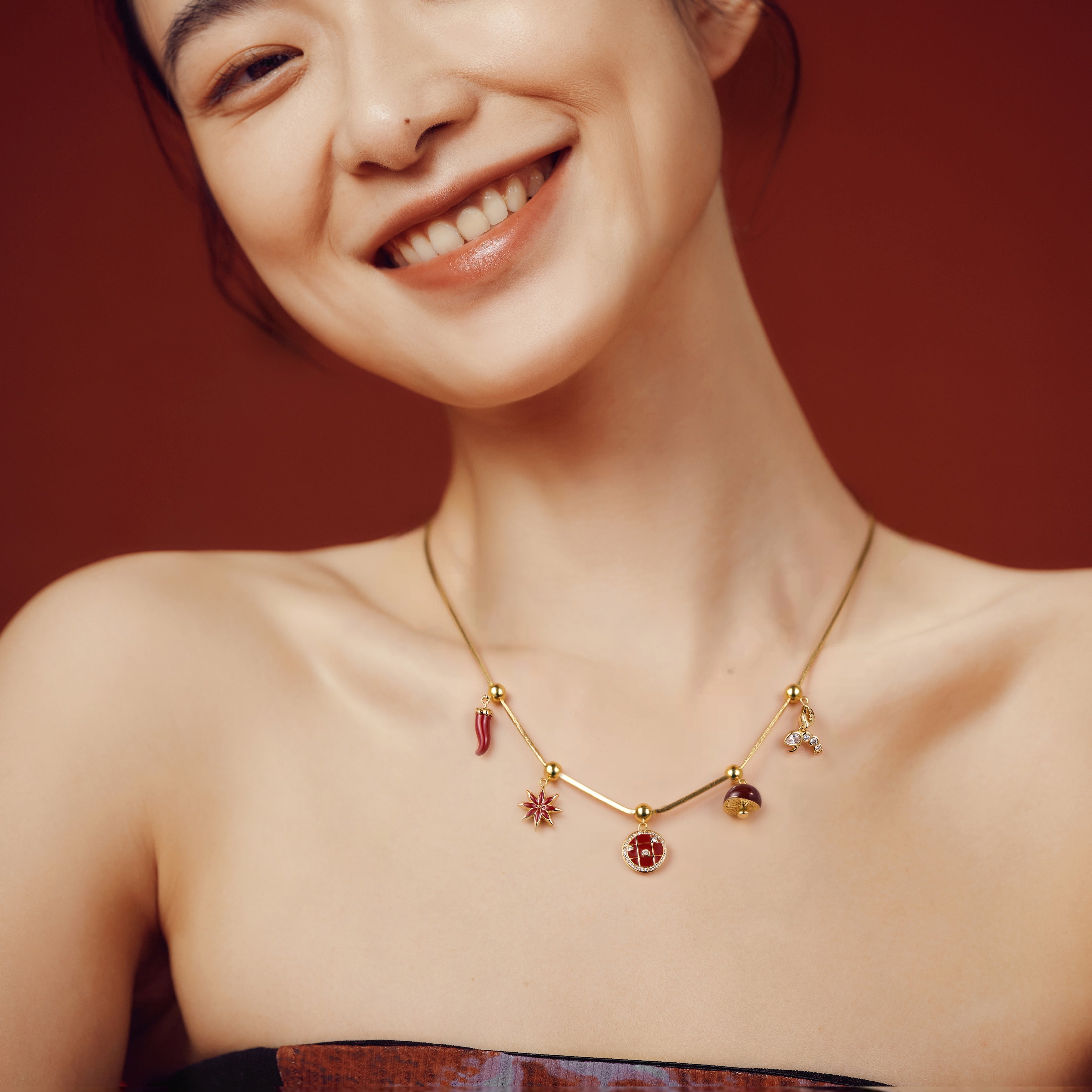 Smiling woman wearing gold-plated charm necklace with red and star pendants