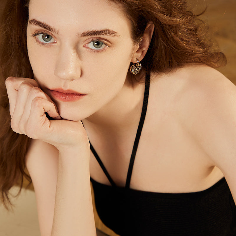 Woman wearing statement gold-plated earrings and a black strappy top, close-up portrait