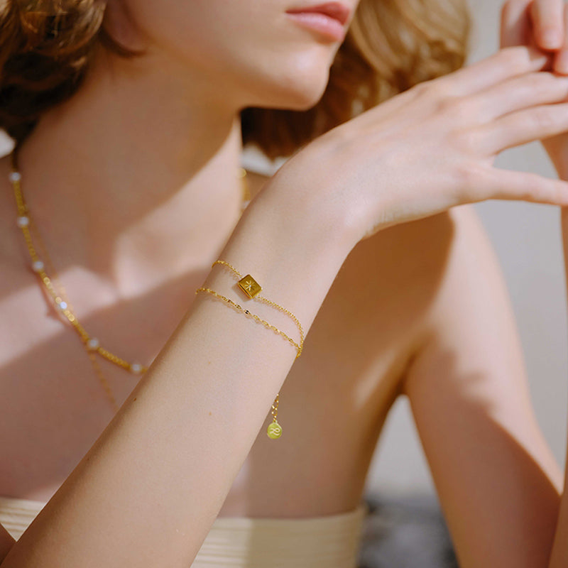 Woman wearing gold-plated layered bracelet with geometric charm and delicate gold necklace