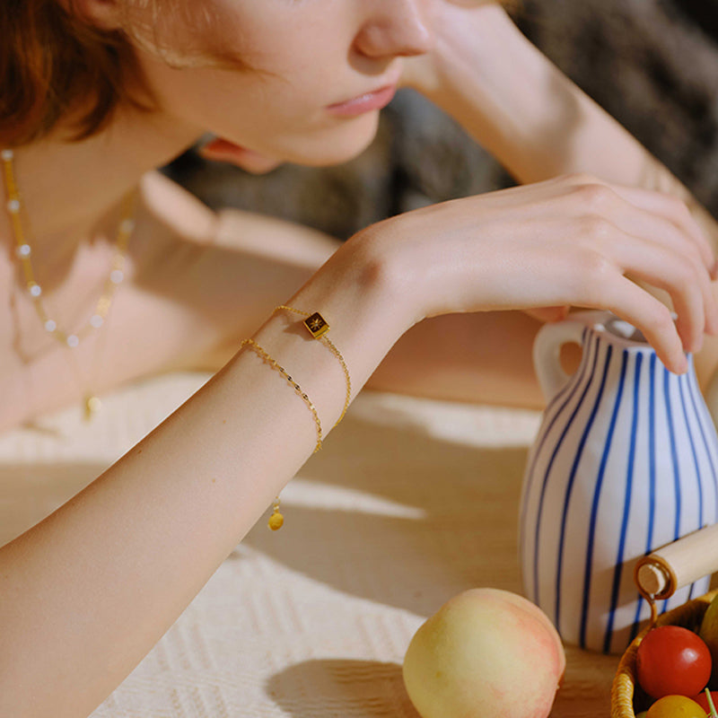 Woman wearing gold-plated bracelet and necklace, resting arm on striped ceramic jug
