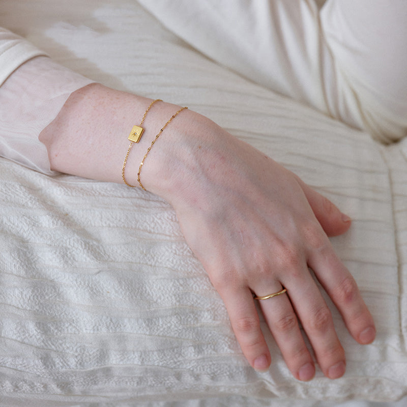 Woman wearing delicate gold-plated bracelets and a simple gold ring on a white fabric background