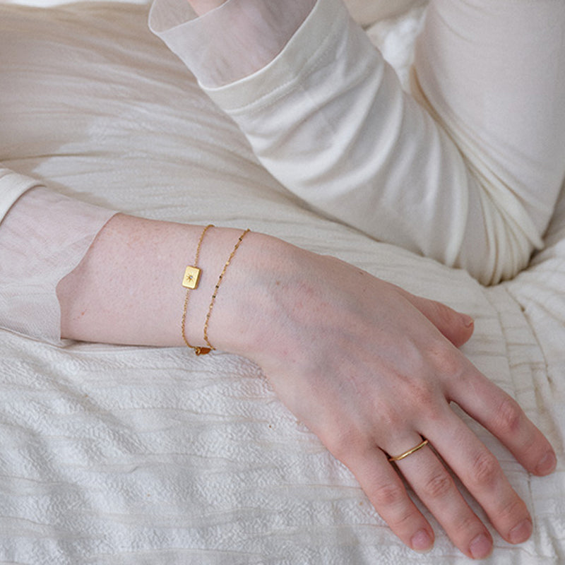 Woman wearing delicate gold-plated bracelets and a thin gold ring on a cream fabric